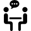 Two people sat either side of a desk facing each other in discussion